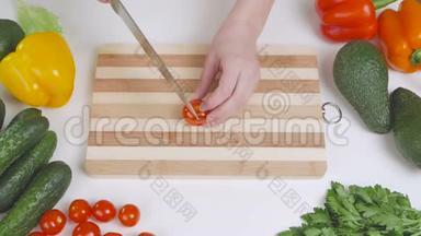 一个女人在分割的木板上用刀切一个樱桃番茄。